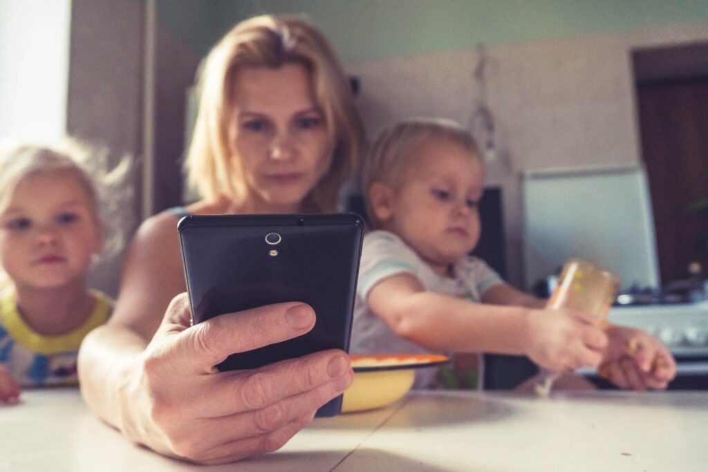 A working parent checks her phone while holding her child